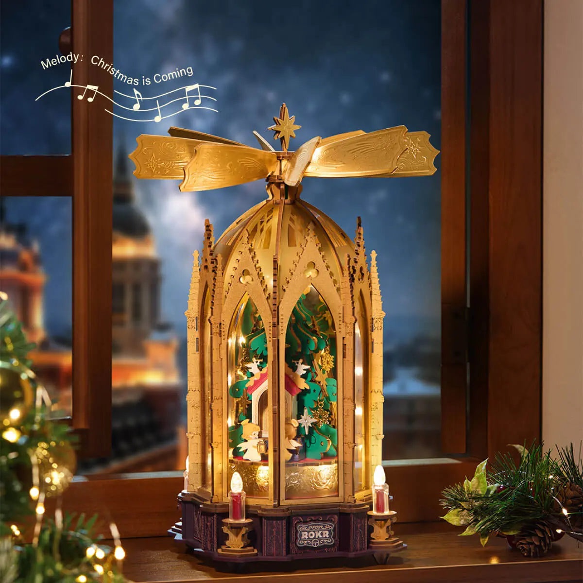 ROKR AMB01 Christmas pyramid beside a winter window, with musical notes naming the melody “Christmas is Coming”