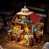 Rolife Clockwise Clocks DH104 miniature house illuminated beside stacked books, showing its red roof and detailed workshop.