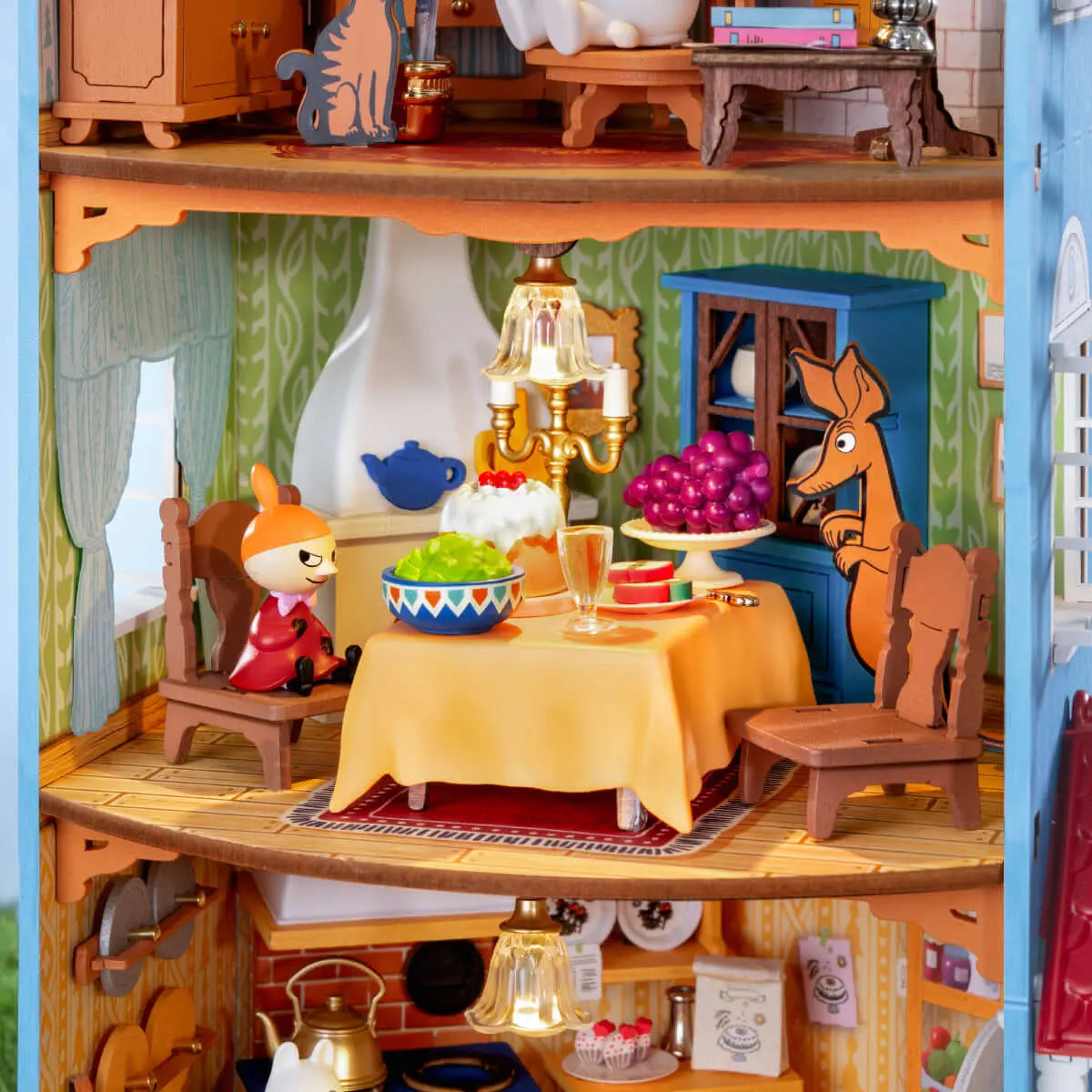 Close-up of the Moominhouse dining room with Little My, a set table, fruit and a lit chandelier
