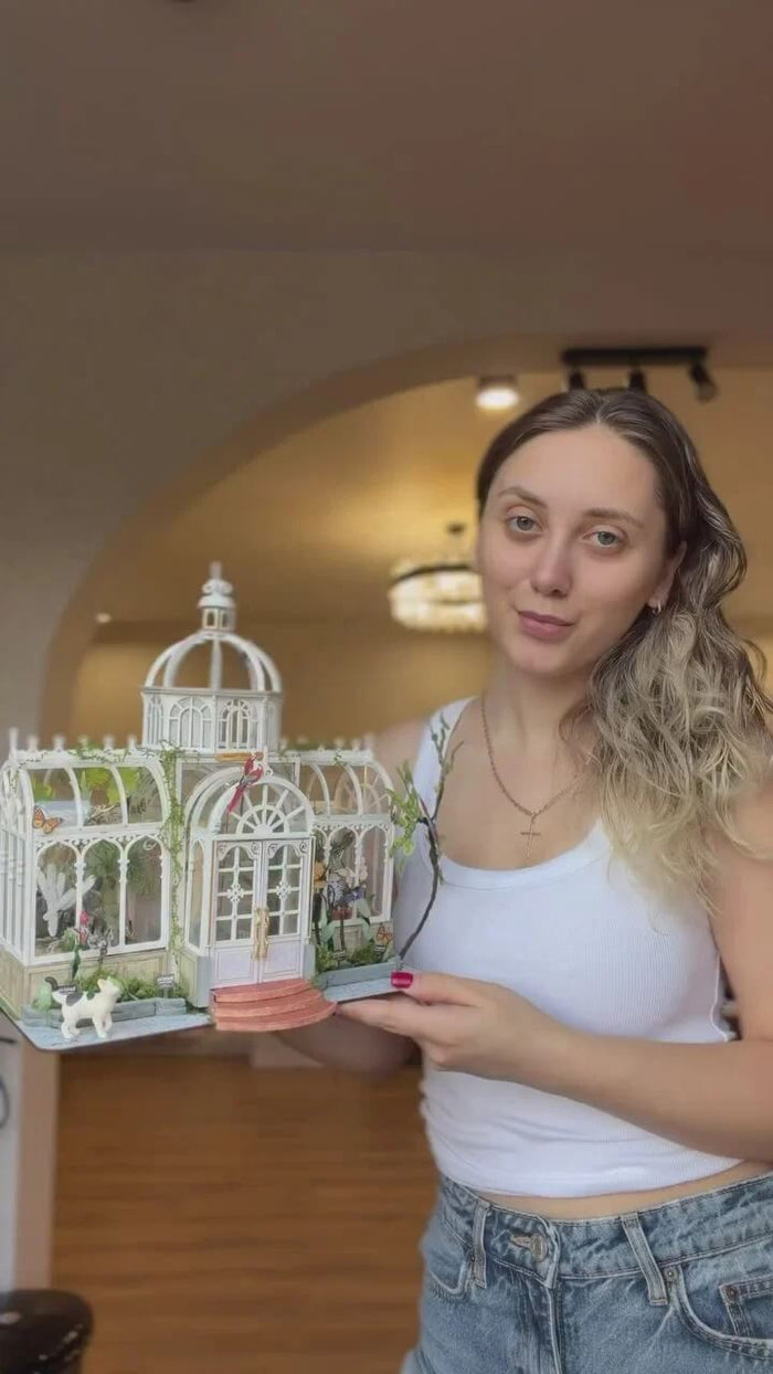 Builder displaying a completed white DIY miniature greenhouse house kit
