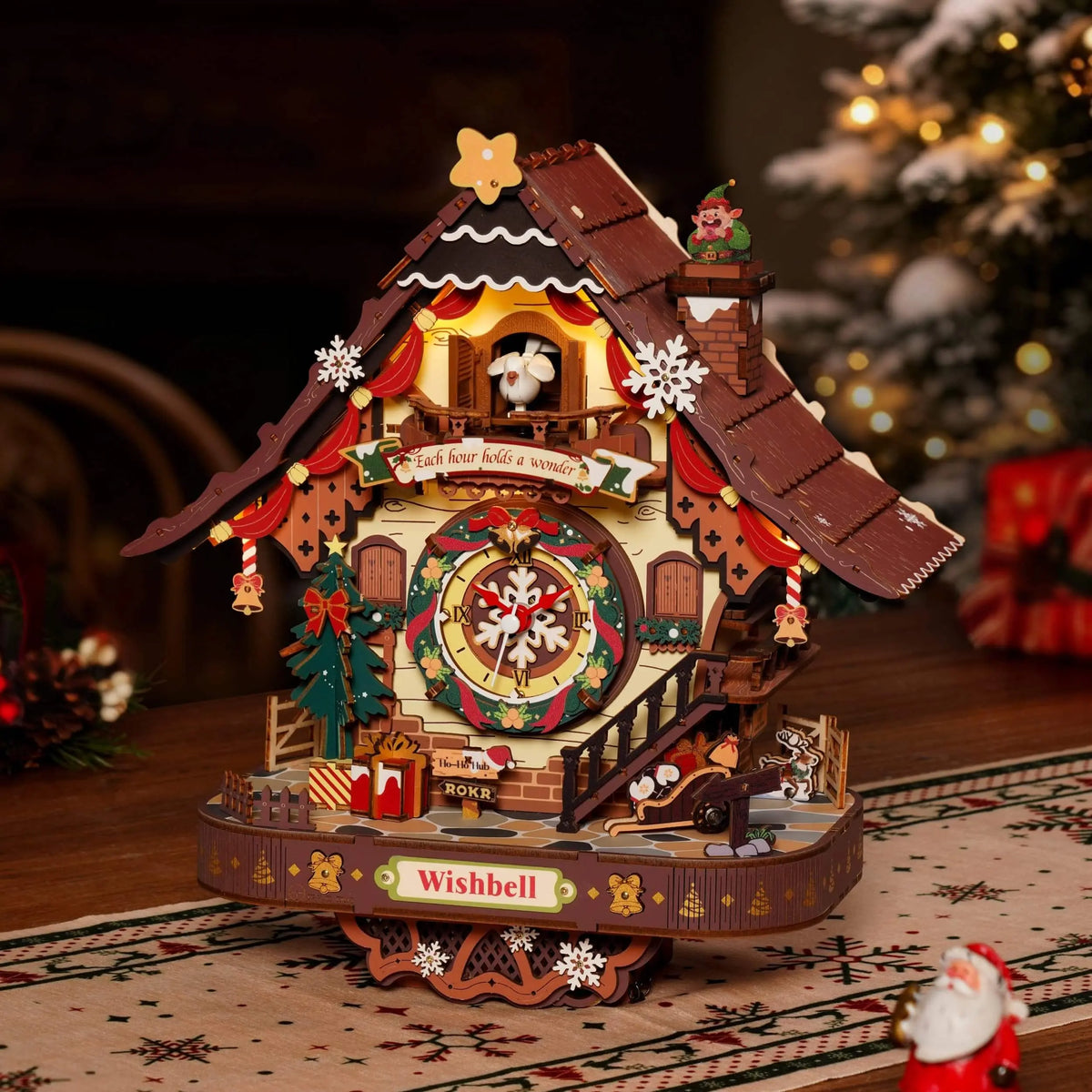 ROKR LCB01 Christmas cuckoo clock glowing on a wooden tabletop with a Christmas tree and gifts in the background.